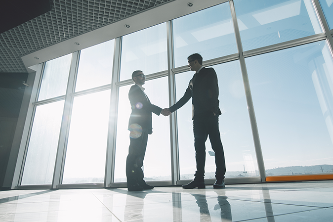 Two businessmen shaking hands in front of office building windows