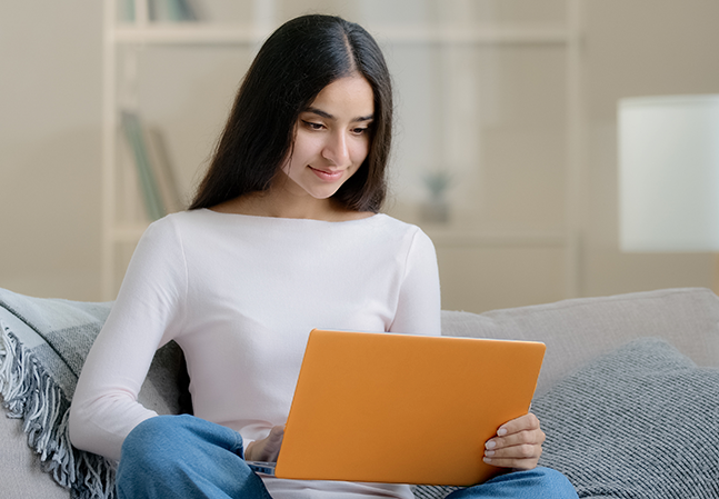 Young woman sitting on couch working on laptop