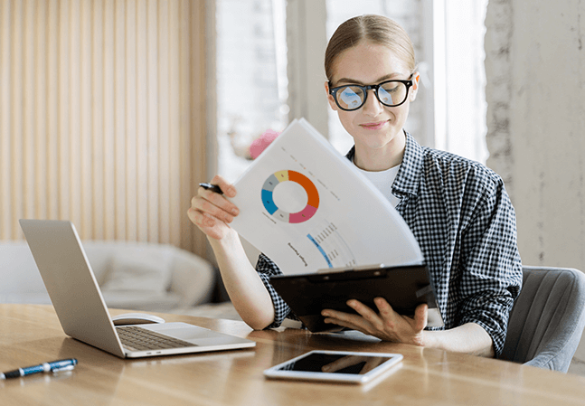 Young woman wearing glasses looking over financial paperwork at a desk with a laptop