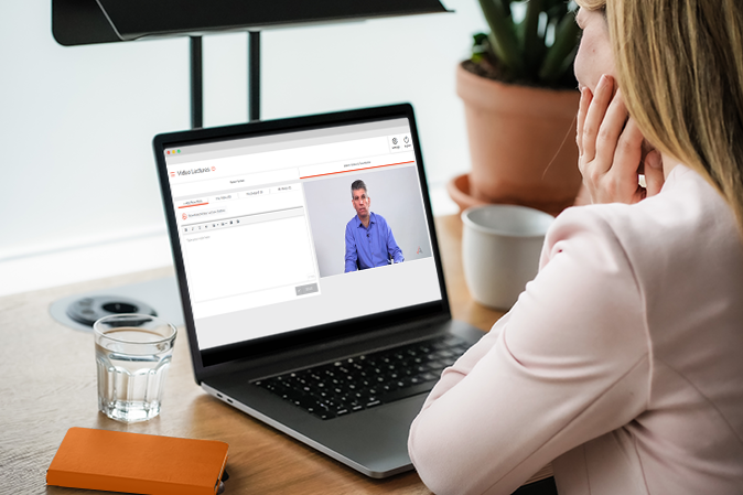 Woman sitting at a desk watching a Jonathan Grossman video lecture on her laptop