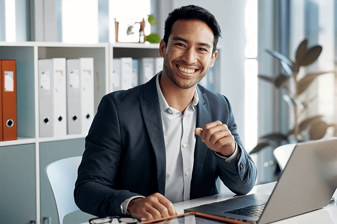 Young man dressed in a suit smiling in front of a laptop