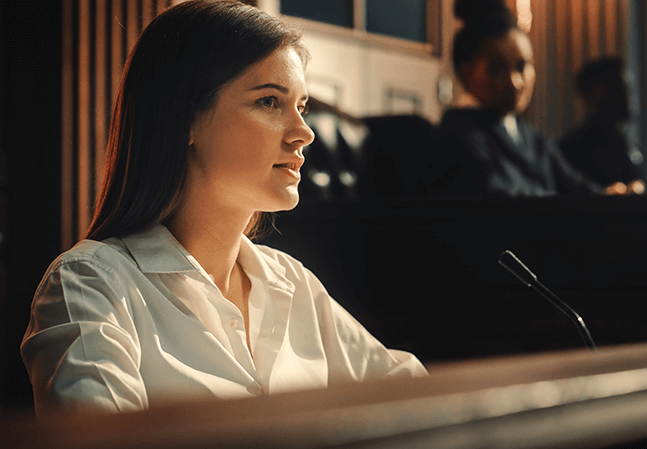 Young woman being questioned in a courtroom next to a judge