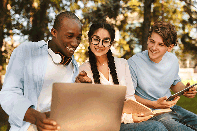 Group of three students outside working together on a laptop