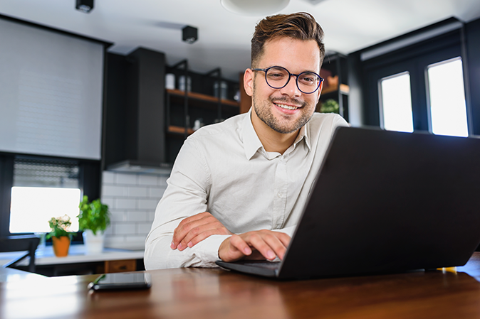 Young man smiling sitting at a desk working on a laptop