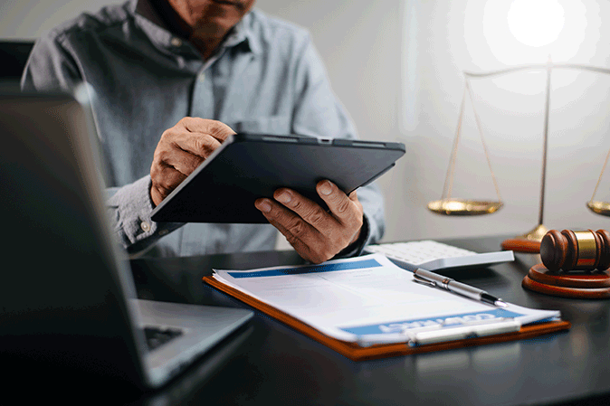 Man working on a tablet at his desk with a gavel and contract on a clipboard