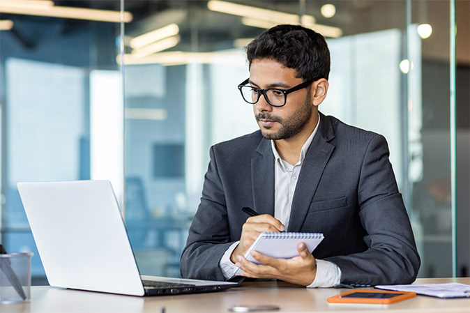 Young man taking notes in front of a laptop in an office