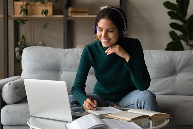 Smiling woman wearing headphones studying online at home sitting on couch