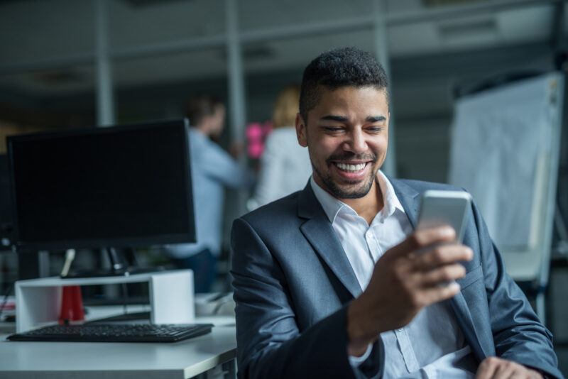 Happy african american businessman using a mobile phone in an office.