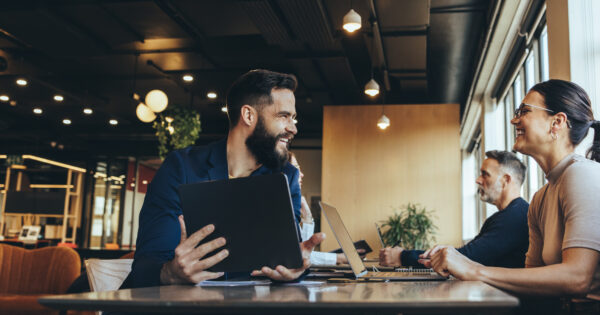 Co-workers smiling at each other while sitting at a table in a co-working space. Two happy businesspeople sharing a workspace in an open office. Cheerful young entrepreneurs using wireless technology.